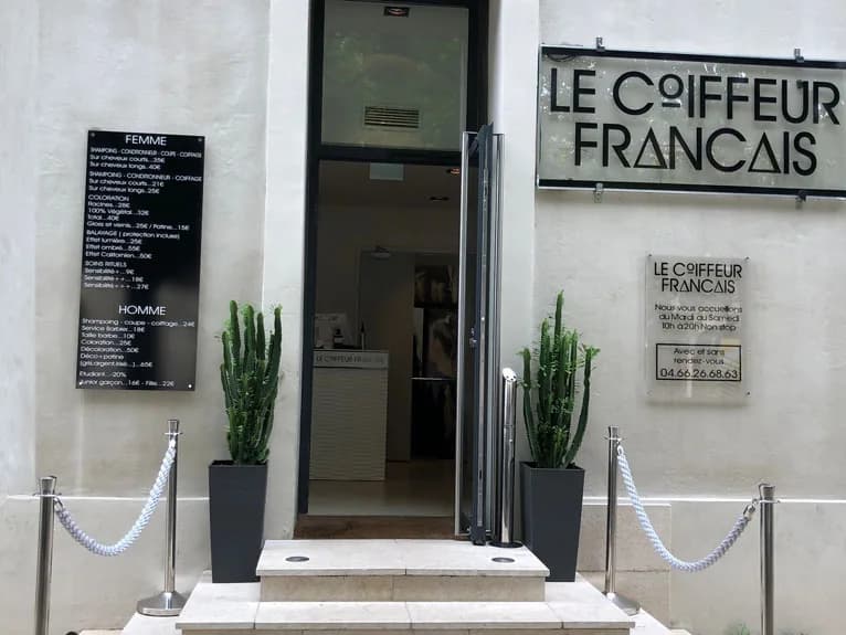 L’entrée du salon Le Coiffeur Français à Nîmes, enseigne noire sur mur clair, deux cactus de part et d’autre de la porte vitrée.