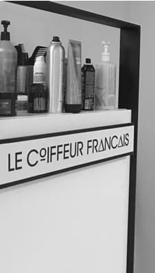 Une étagère de produits capillaires au-dessus d’un poste de coiffage portant le nom du salon.